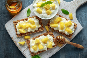Homemade Crispbread toast with Cottage Cheese, Pineapple and honey on white wooden board.