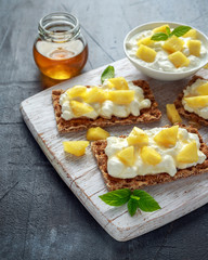 Homemade Crispbread toast with Cottage Cheese, Pineapple and honey on white wooden board.