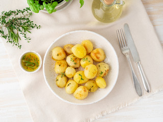baked in oven with spices round whole potato tubers in plate on white textile background, golden with crust, top view