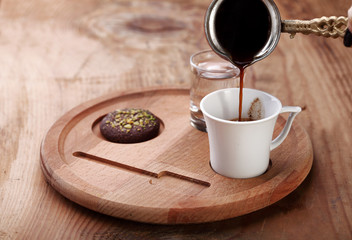 pooring turkish coffee in to a cup with cookie on a wooden background