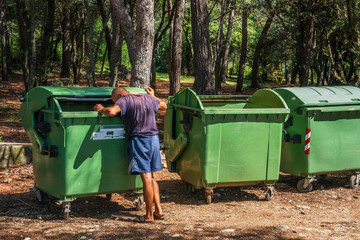 Homeless digging in green dumpsters in the city, summer Sunny day