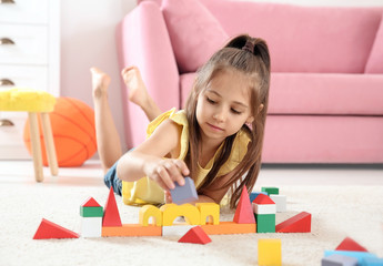 Cute little child playing with building blocks on floor, indoors