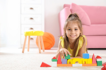 Cute little child playing with building blocks on floor, indoors