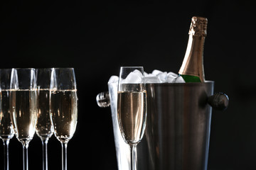 Glasses with champagne and bottle in bucket against dark background