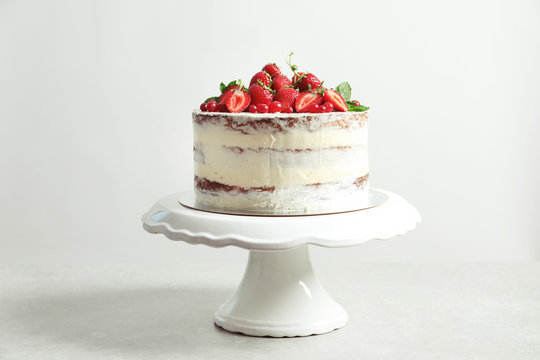 Delicious homemade cake with fresh berries on stand against light background