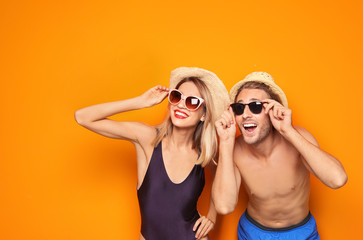 Happy young couple in beachwear and sunglasses on color background