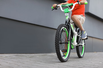 Little boy riding bicycle on street near gray wall, closeup
