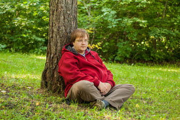 Naklejka premium Thick man sitting on the grass in the park
