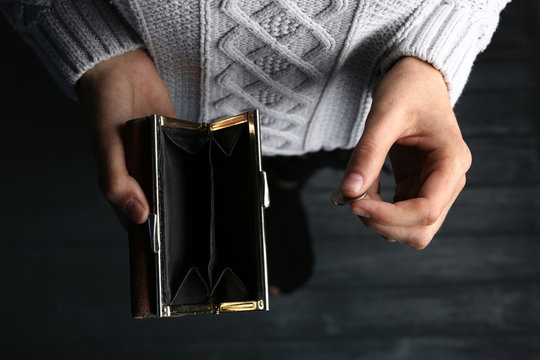 Poor woman holding empty wallet and coin on wooden background, closeup