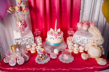 Sweet table and big unicorn cake for baby girl first birthday. Candy bar with a lot of different candies and sweet cakes