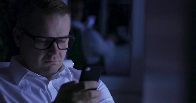 Tired sleepy man - workaholic is trying to write message home on smart phone in night office