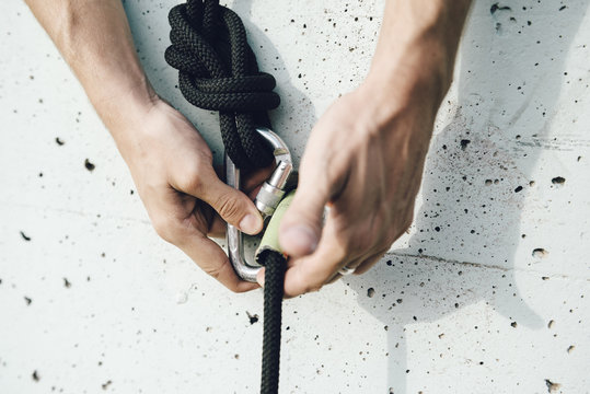 Hands securing a climbing rope with a carabiner on a concrete wall