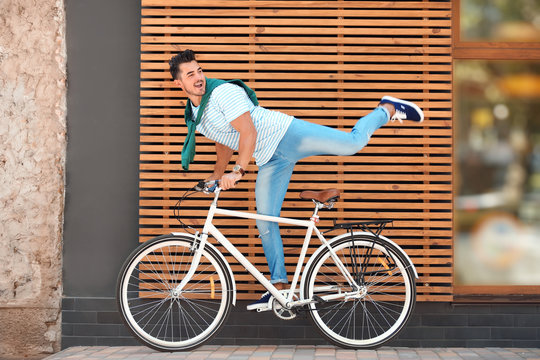 Handsome young hipster man with bicycle near wooden wall outdoors