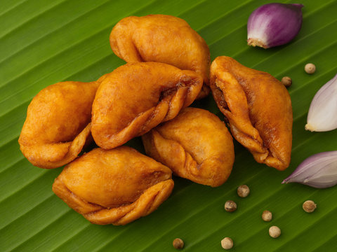 Packshot close up view of "Pan Klib" traditional mini Thai puff dessert stuffed material with fish, curry, shallot, pepper seasoned sugar and salt on green banana leaf