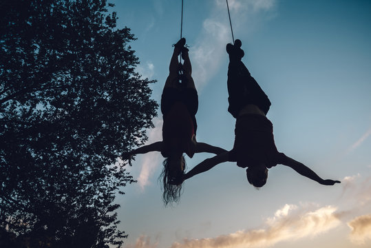Silhouette of couple of aerial dancers performing a choreography on urban scenery at sunset