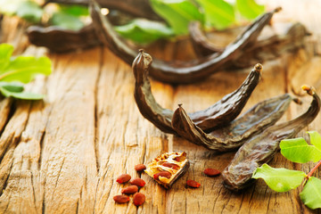 Carob. Healthy organic sweet carob pods with seeds and leaves on a wooden table. Healthy eating, food background