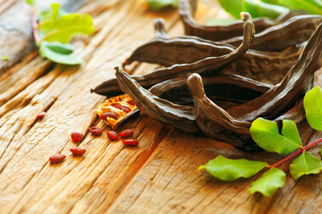 Carob. Healthy organic sweet carob pods with seeds and leaves on a wooden table. Healthy eating, food background