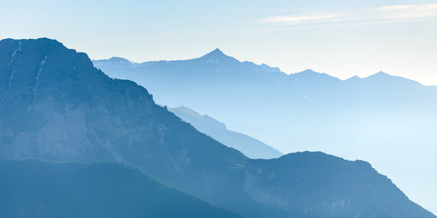 Distant blue toned mountain range of the majestic European Alps with mist and fog in the valley below