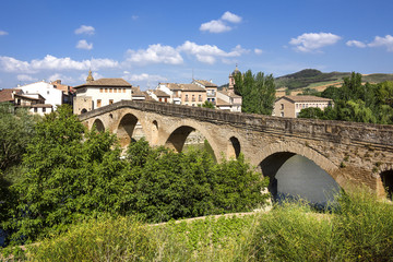 Spain, Puente La Reina, Gares: Panoramic view of famous romanesque bridge over river Arga with skyline of Spanish small town literally named 'Bridge of the Queen', green riverside and blue sky.