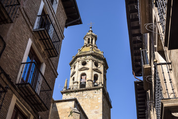 Fototapeta na wymiar Spain, Puente La Reina, Gares: Steeple of famous old Iglesia del Crucifijo church with skyline of Spanish small town literally named 'Bridge of the Queen', house facades and blue sky in background.
