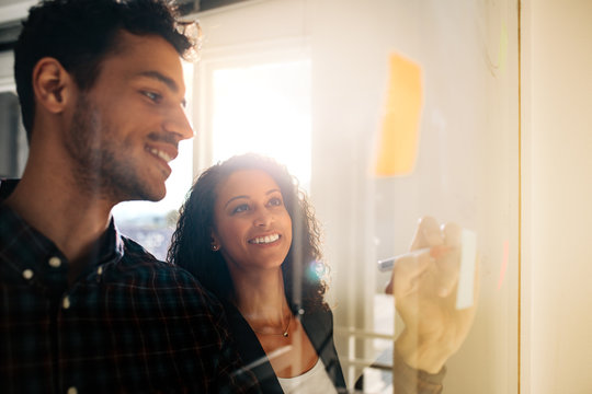 Business colleagues discussing ideas on glass board in office