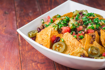 A plate of delicious nachos with jalapeno, beans and guacamole sauce