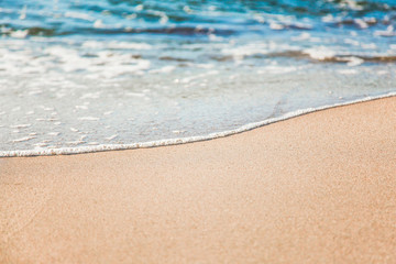 waves of pure azure water with white foam on yellow sand on a sunny day, close up blurry background