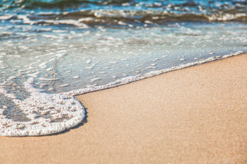 waves of pure azure water with white foam on yellow sand on a sunny day, close up blurry background