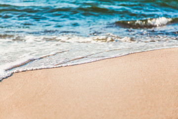 waves of pure azure water with white foam on yellow sand on a sunny day, close up blurry background