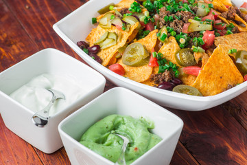 A plate of delicious nachos with jalapeno, beans and guacamole sauce