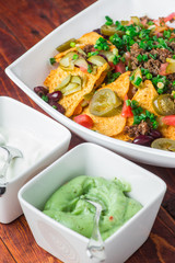 A plate of delicious nachos with jalapeno, beans and guacamole sauce