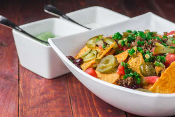 A plate of delicious nachos with jalapeno, beans and guacamole sauce