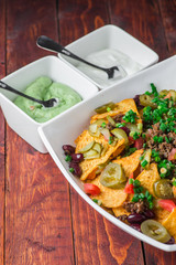 A plate of delicious nachos with jalapeno, beans and guacamole sauce