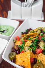 A plate of delicious nachos with jalapeno, beans and guacamole sauce