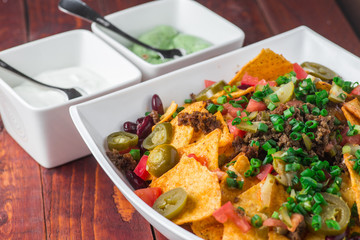 A plate of delicious nachos with jalapeno, beans and guacamole sauce