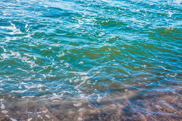 Fototapeta na wymiar pure azure clear water with white foam on the sea on a sunny afternoon, blurry background