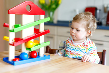 Adorable cute beautiful little baby girl playing with educational toys at home or nursery. Happy healthy child having fun with colorful wooden toy ball track. Kid learning to hold and roll ball.