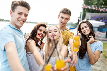 A company of good-looking friends laughing and drinking yellow cocktails and socialising  in the nice cafe next to the river. Cheers. Entertainment, having good time. River is in the background.