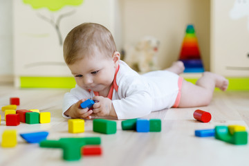 Cute happy smiling baby playing with colorful rattle toys. New born child, little girl learning crawling. Family, new life, childhood, beginning concept. Baby learning grab wooden blocks.