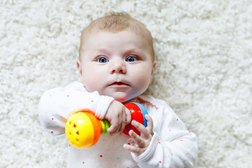 Cute adorable newborn baby playing with colorful rattle toy on white background. New born child, little girl looking at the camera. Family, new life, childhood, beginning concept. Baby learning grab.