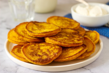 Homemade pumpkin pancakes served with sour cream on a light background.