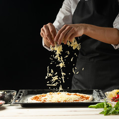 The chef sprinkles the pizza with cheese on a dark background, with free space