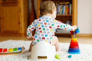 Closeup of cute little 12 months old toddler baby girl child sitting on potty. Kid playing with...