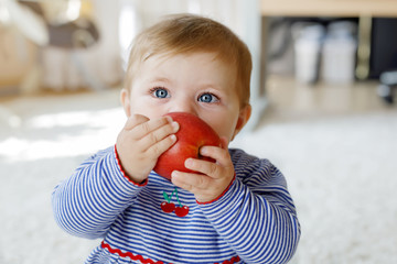 Little adorable baby girl eating big red apple. Vitamin and healthy food for small children....