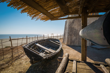 The wooden well, old holey boat and dilapidated hut on the seashore on a sunny day