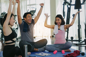 group of young sporty people high fiving and laughing together sitting on yoga mat in fitness gym after workout, exercise at morning, training, workout, partnership, success and teamwork concept
