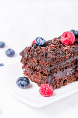 Chocolate pie with raspberries and blueberries on a white saucer on a white wooden background	