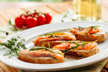 Whole grain bread with avocado paste and salmon decorated with arugula. Side close view with cherry tomatoes on background