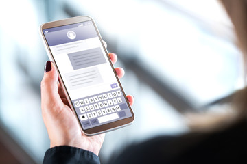 Woman sending text messages with mobile phone. Cellphone in hand with sms application on screen. Person using instant messaging software with smartphone. Texting and digital communication concept.