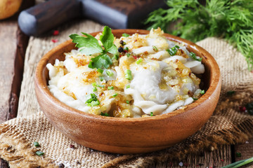 Traditional Russian vareniki with potatoes and fried onions in bowl on old wooden table, rustic style, selective focus